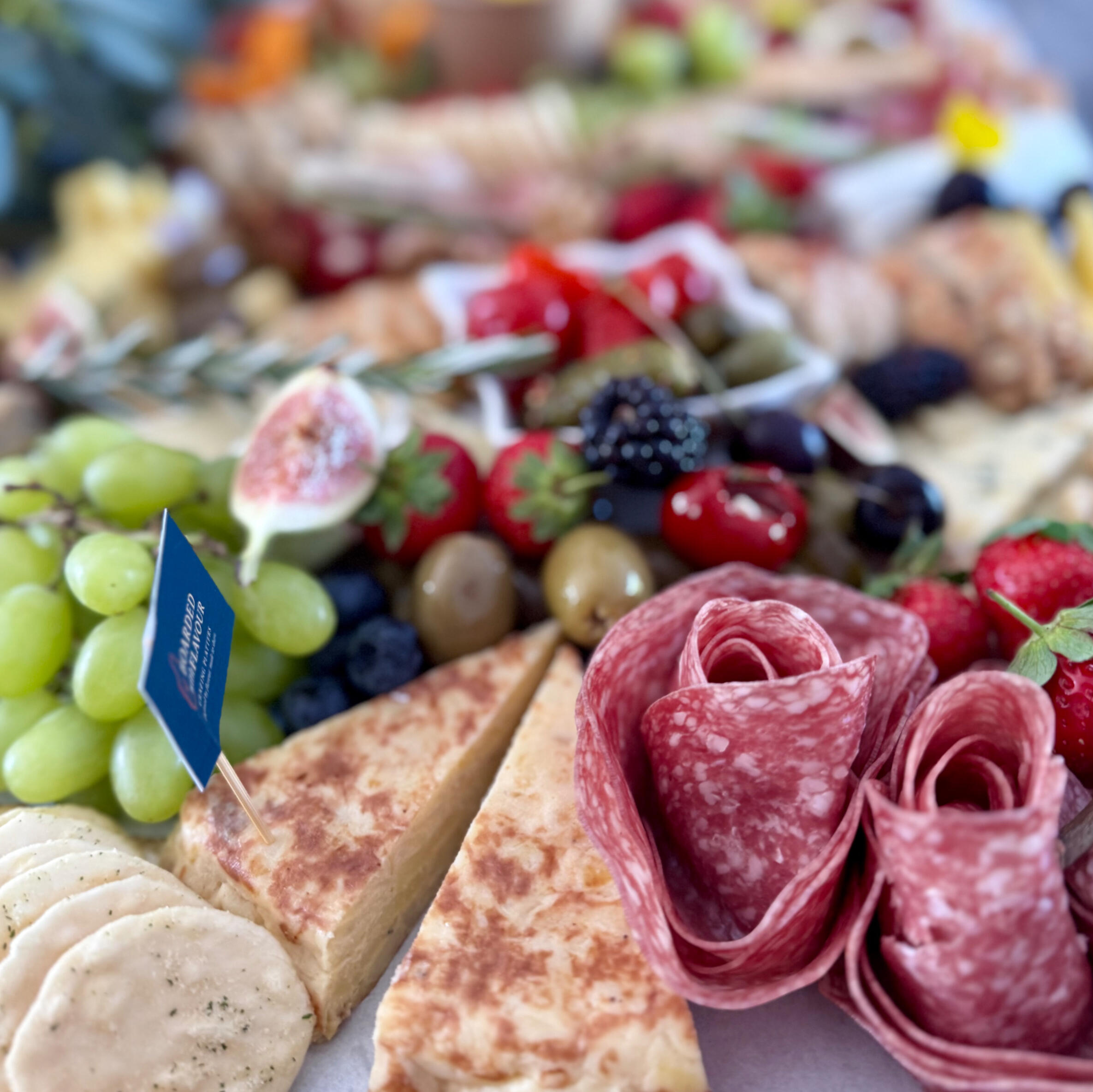 A close up of some charcuterie a close up of some grapes, blackberries, meats, tortilla and stuffed peppers